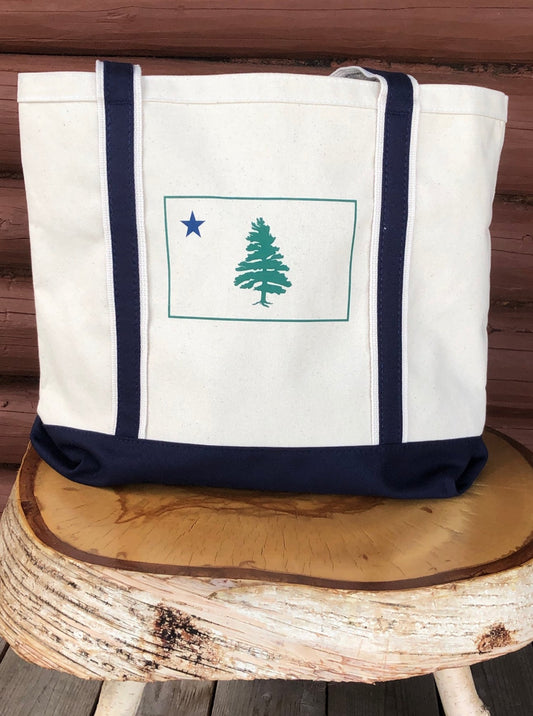 Large boat bag with 1901 original Maine flag screen printed on the front. Natural cream bag with navy straps and bottom. Made in USA. Bag is displayed on a birch log stool on a log cabin porch.